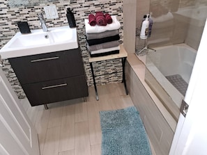 A modern bathroom with a sink, dark wooden cabinet, a small table with towels, and a shower area. - Amazing 3 Bedrooms With 3 Bedroom apt in the Center of Beverly Hills (Beverly Hills)