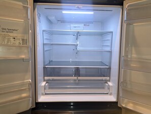 Egy üres hűtőszekrény, melynek polcai fel vannak címkézve, külön a gyümölcsök és a zöldségek számára, friss levegőszűrővel és vízadagolóval felszerelve.