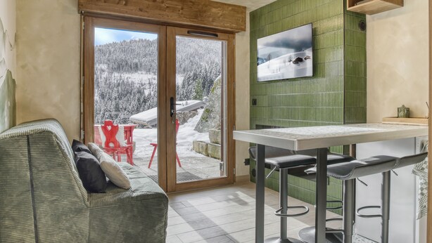 Una habitación acogedora con un sofá, una mesa de comedor y vistas a un paisaje nevado a través de una puerta corrediza.