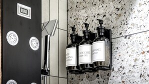 Un baño con una puerta negra, un espejo y una ducha. Hay tres botellas de gel de ducha en una estantería.