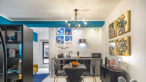 A modern kitchen with a dining area, featuring a chandelier, artwork, and a bookshelf. - Ca' Petunia Art Apartment R&R (Venecia)
