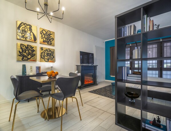 A modern living room with a fireplace, a dining area with a table and chairs, and a bookshelf filled with books. - Ca' Petunia Art Apartment R&R (Venecia)