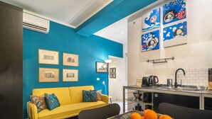 A modern kitchen with a black countertop, a sink, and a coffee maker. There is a yellow sofa with blue cushions and a blue rug on the floor. - Ca' Petunia Art Apartment R&R (Venecia)