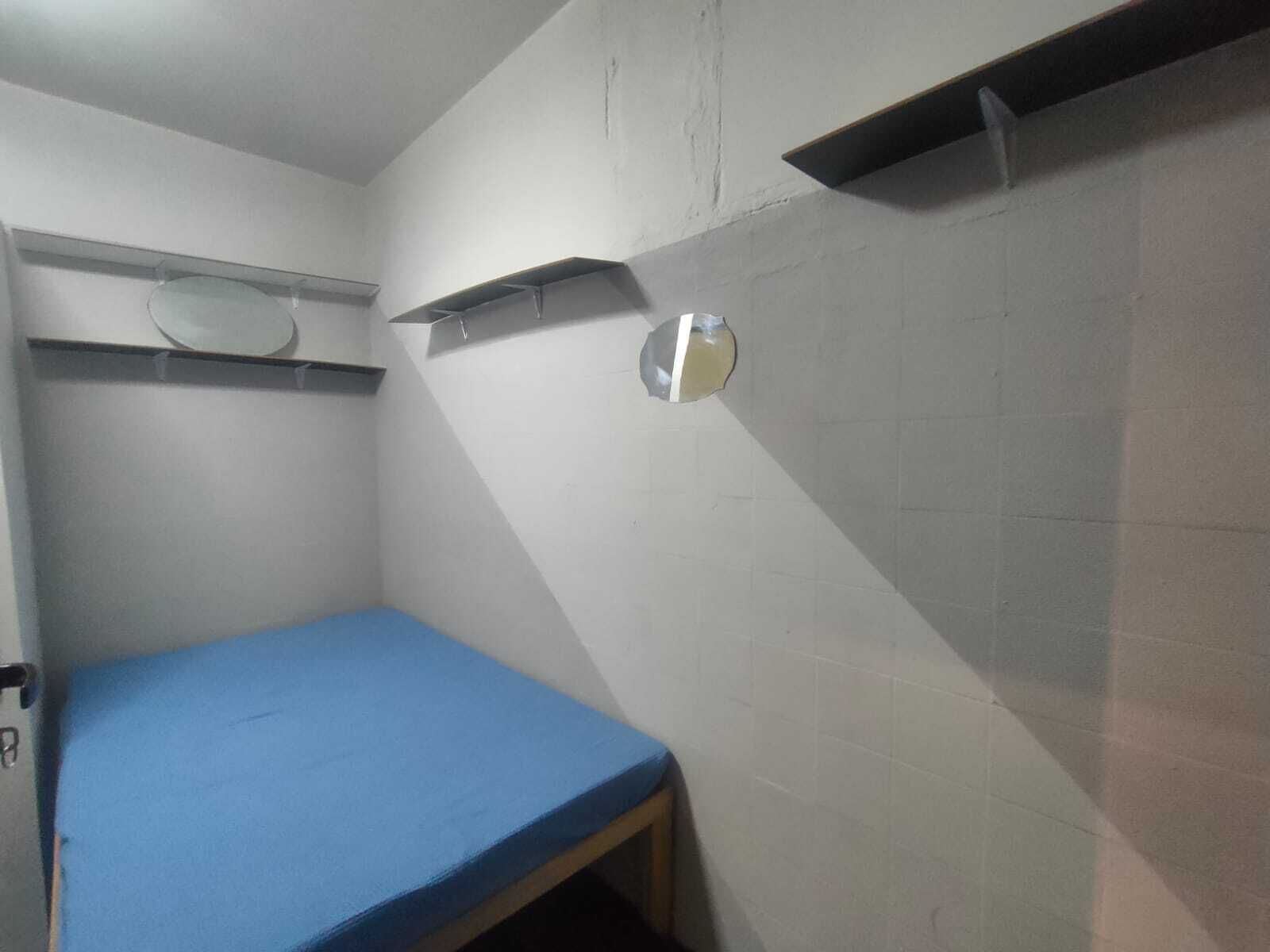 Una habitación pequeña y estrecha con una cama individual, una estantería y un espejo en la pared.