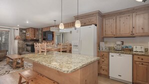 Una cucina con mobili in legno, piani in granito, un'isola centrale con sgabelli, forno a incasso, frigorifero e lavastoviglie.