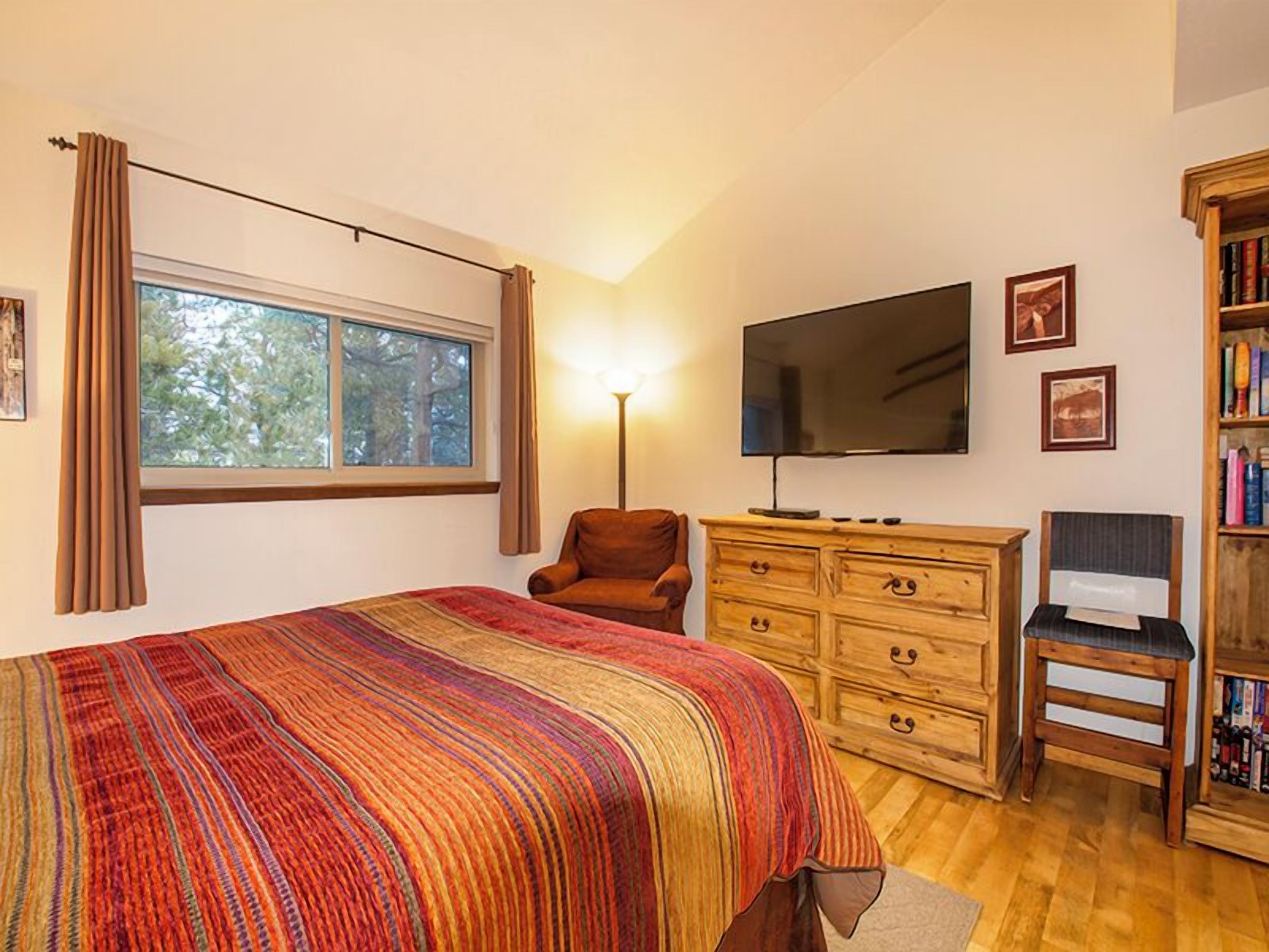 Une chambre à coucher avec un grand lit, une télévision, une commode en bois, une chaise et une bibliothèque.