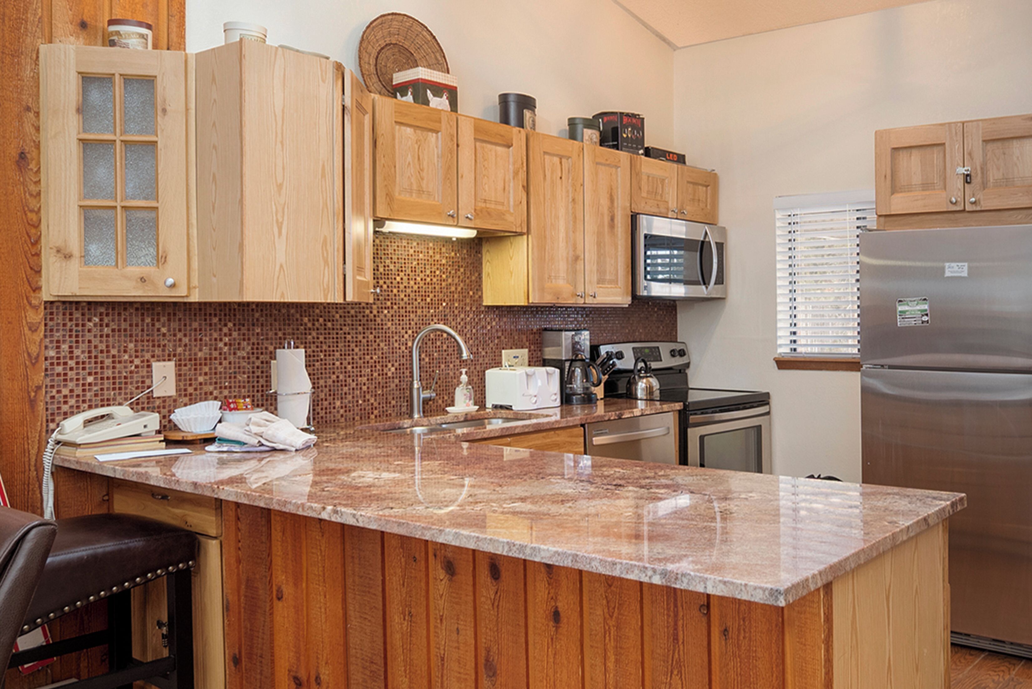A kitchen with wooden cabinets, a granite countertop, a microwave, a refrigerator, and a sink.