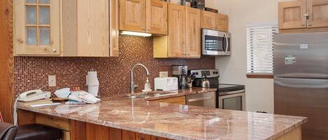 A kitchen with wooden cabinets, a granite countertop, a microwave, a refrigerator, and a sink.