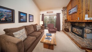 Ein gemütliches Wohnzimmer mit braunem Sofa, einem Holztisch, einem Kamin aus Stein und gerahmten Bildern an der Wand.
