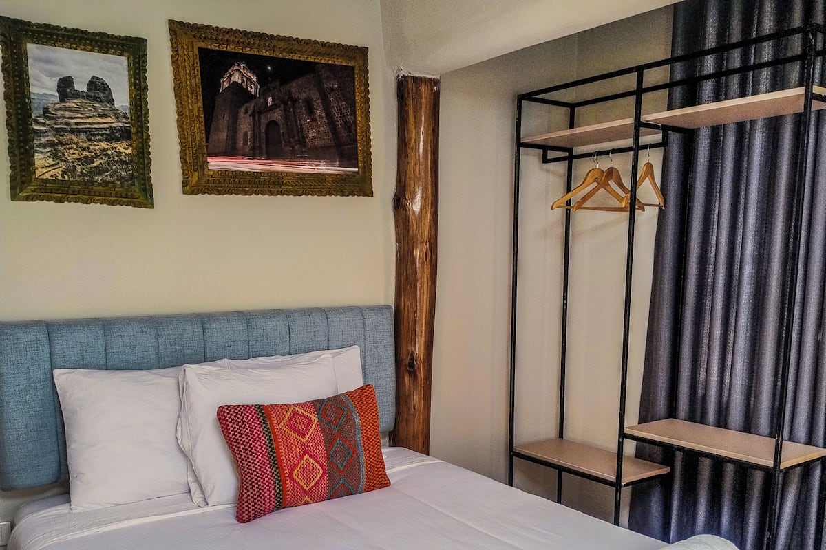 A hotel room with a bed, pillows, a wooden headboard, a wardrobe, and two framed pictures on the wall.