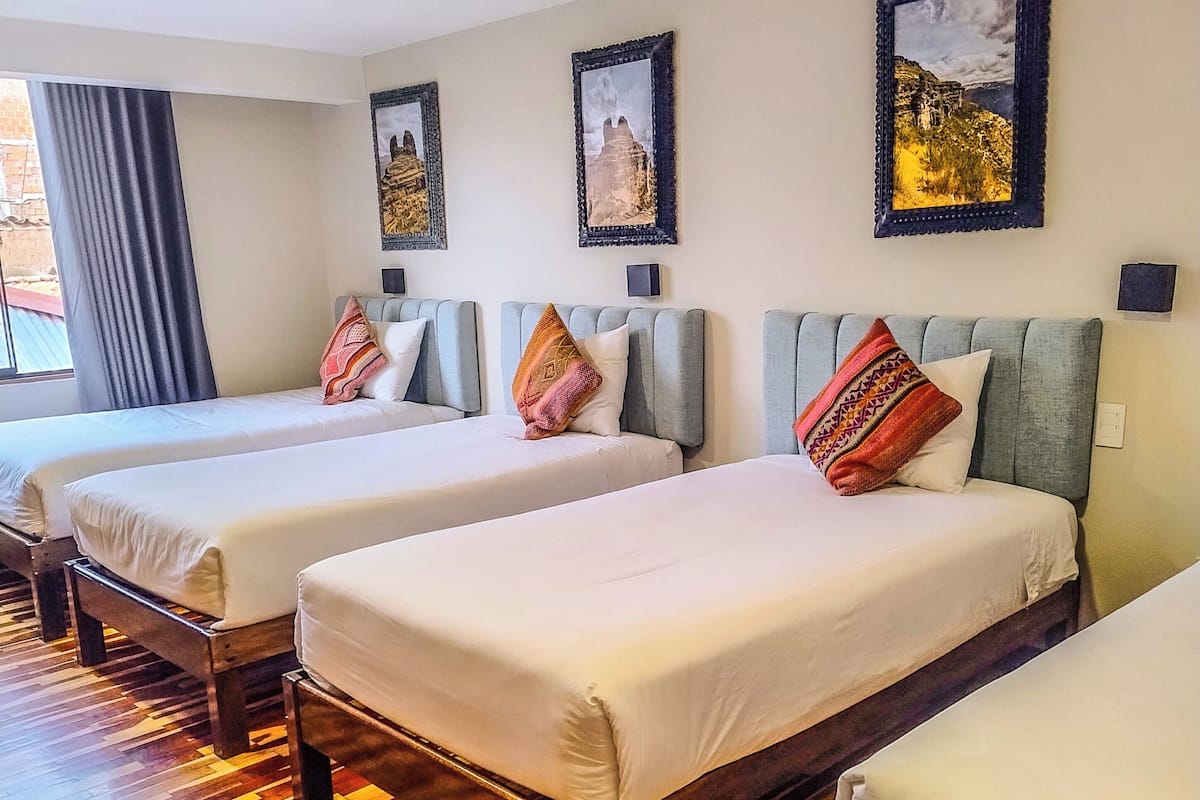 A hotel room with three single beds, wooden flooring, and framed artwork on the walls.