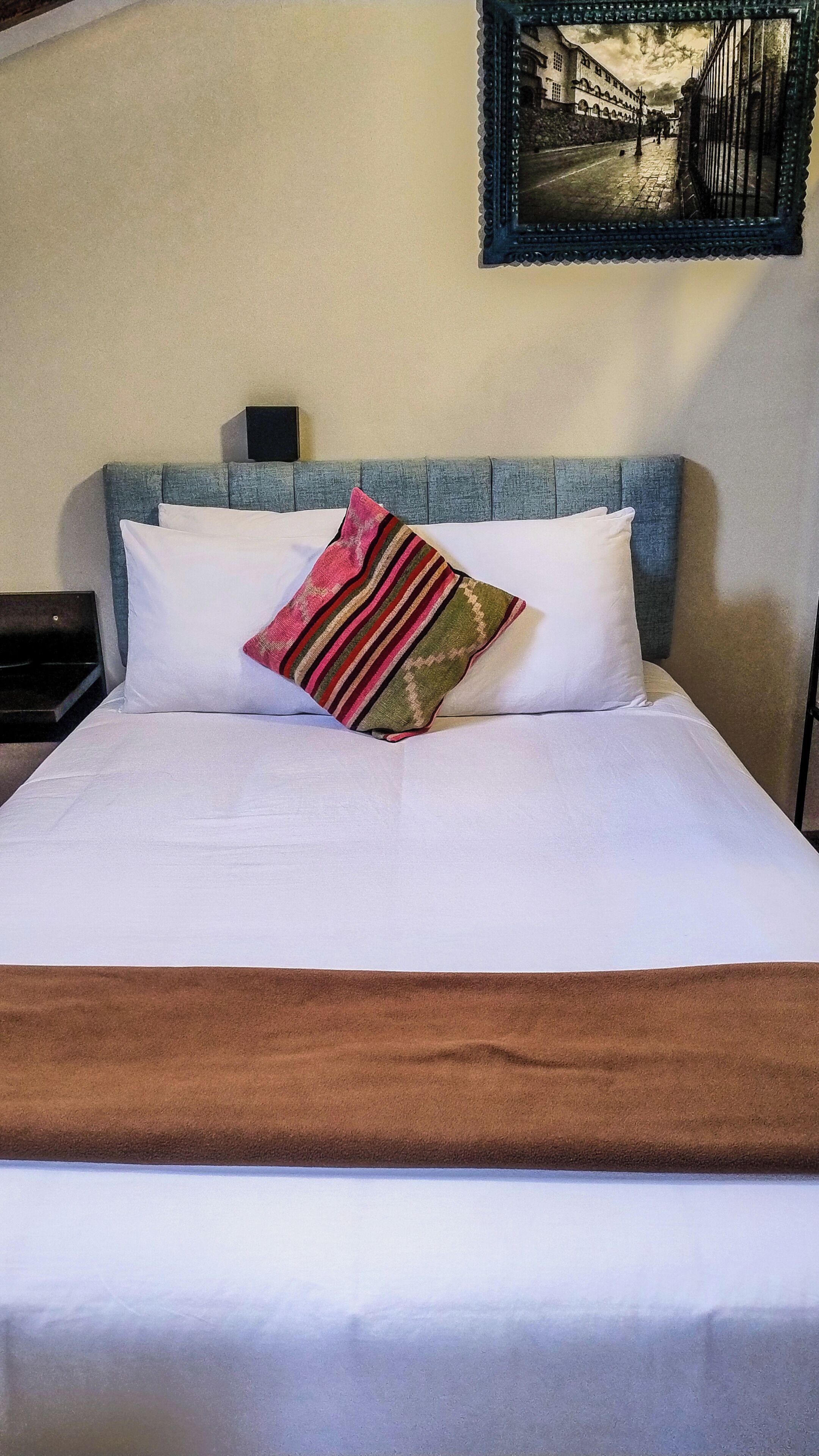 A bed with white linens, a striped pillow, and a brown throw blanket.
