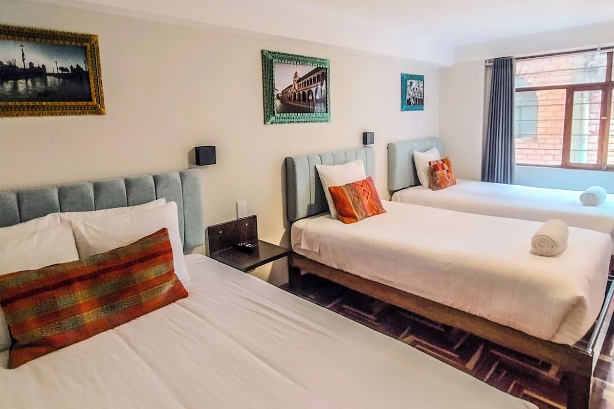 A hotel room with two beds, a nightstand, a lamp, and framed pictures on the wall.