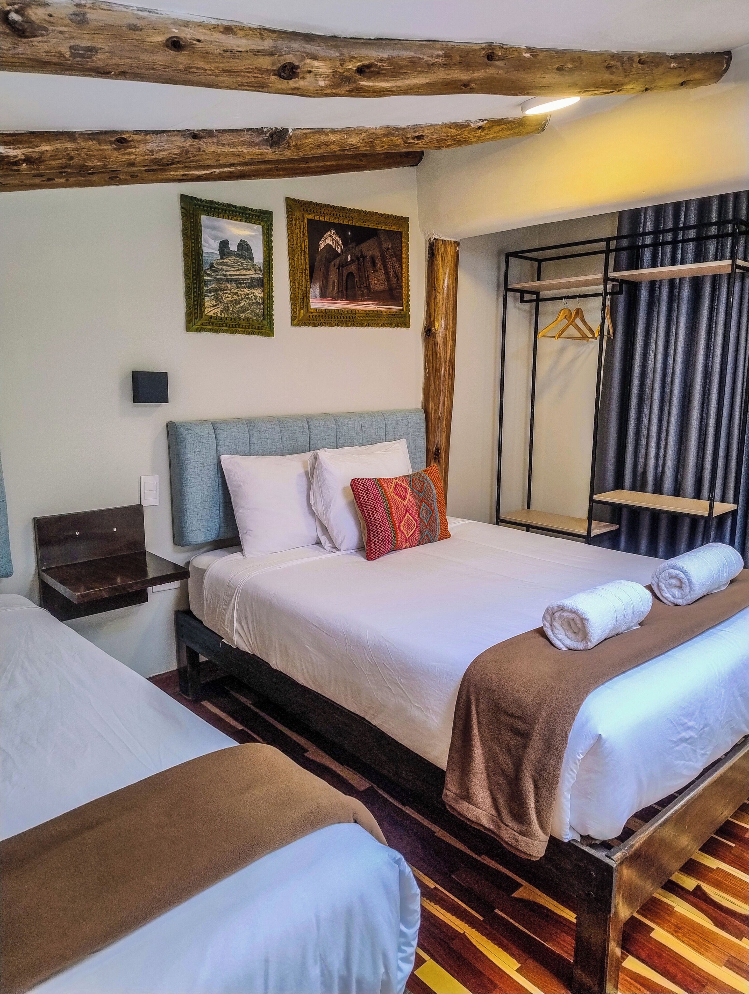 A room with two beds, wooden beams on the ceiling, a wall-mounted coat rack, and a patterned rug.