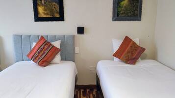 Habitación con dos camas, cada una con un cojín estampado, una pequeña luz fijada a la pared y dos cuadros enmarcados sobre las camas.