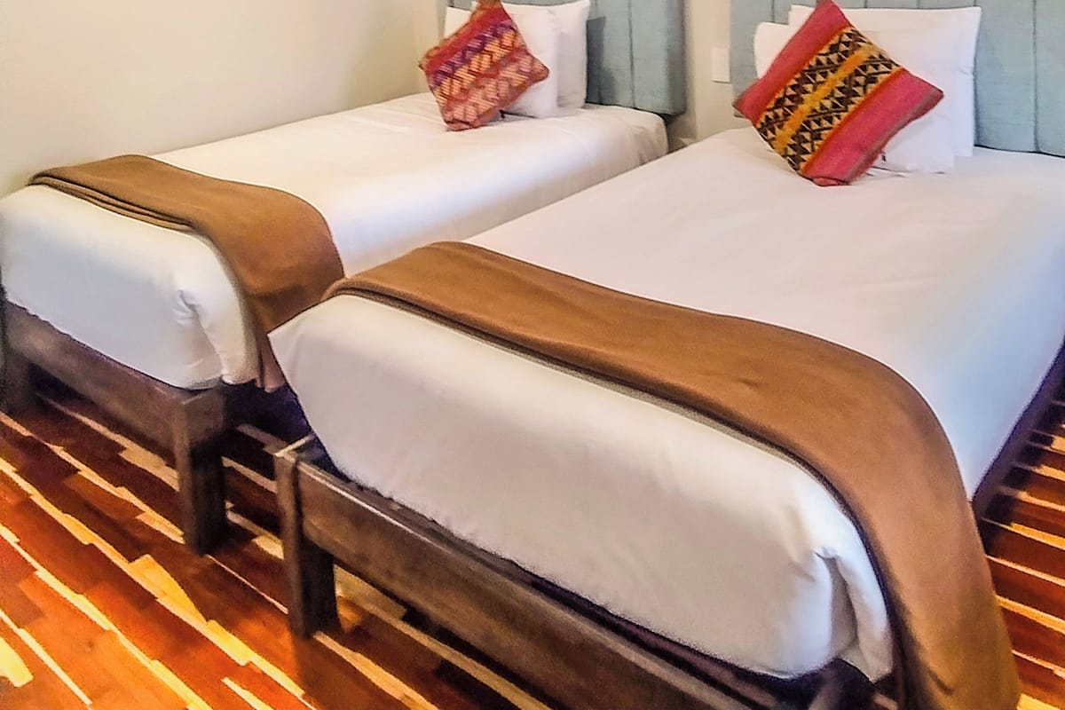 A hotel room with two beds, a wooden chair, a framed picture on the wall, and a patterned floor.