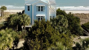 Une maison bleu clair avec un balcon donnant sur la plage et l’océan.
