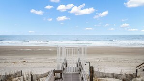 Une promenade en bois mène à une plage agrémentée d’une porte blanche, d’un sable fin et des vagues de l’océan.