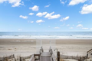 A wooden boardwalk leading to a beach with a white gate, sandy beach, and ocean waves. - Sip by the Sea - Oceanfront, 5-bedrooms (Pawleys Island)
