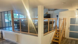 Een modern interieur met een eethoek, grote ramen, een trap en uitzicht op de omgeving.