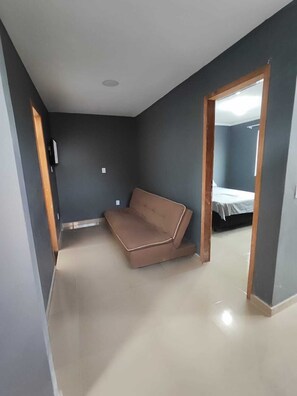 A room with a brown sofa, a bed with a white cover, and a door leading to another room. - One-bedroom apartment with sofa bed. (Rio das Ostras)