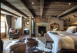 A rustic bedroom with a stone fireplace, wooden beams, a cowhide rug, a bed with white bedding, and a wooden bench. - SmartStay Chalet Ruitor Sainte-Foy-Tarentaise (Sainte-Foy-Tarentaise)
