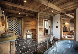 A rustic bathroom with a large bathtub, checkered tiles, wooden beams, and a stone floor. - SmartStay Chalet Ruitor Sainte-Foy-Tarentaise (Sainte-Foy-Tarentaise)