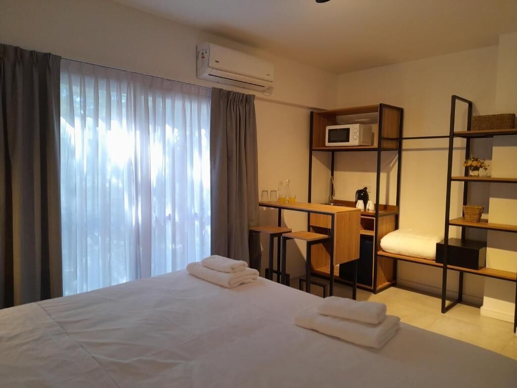 A hotel room with a bed, a desk, a chair, a microwave, and a shelf with a basket.