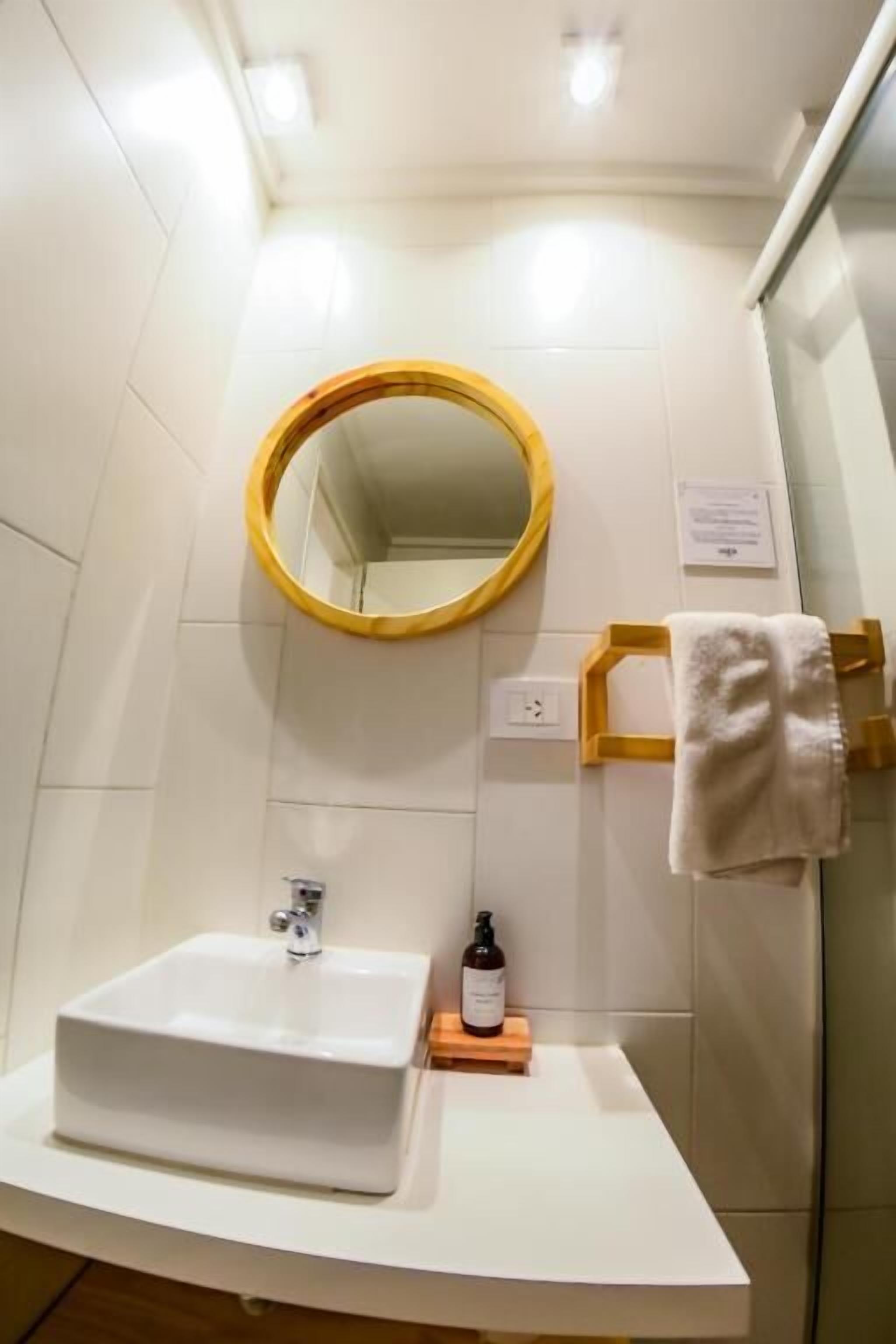 Un baño con un lavabo blanco, un espejo redondo y un perchero para toallas.