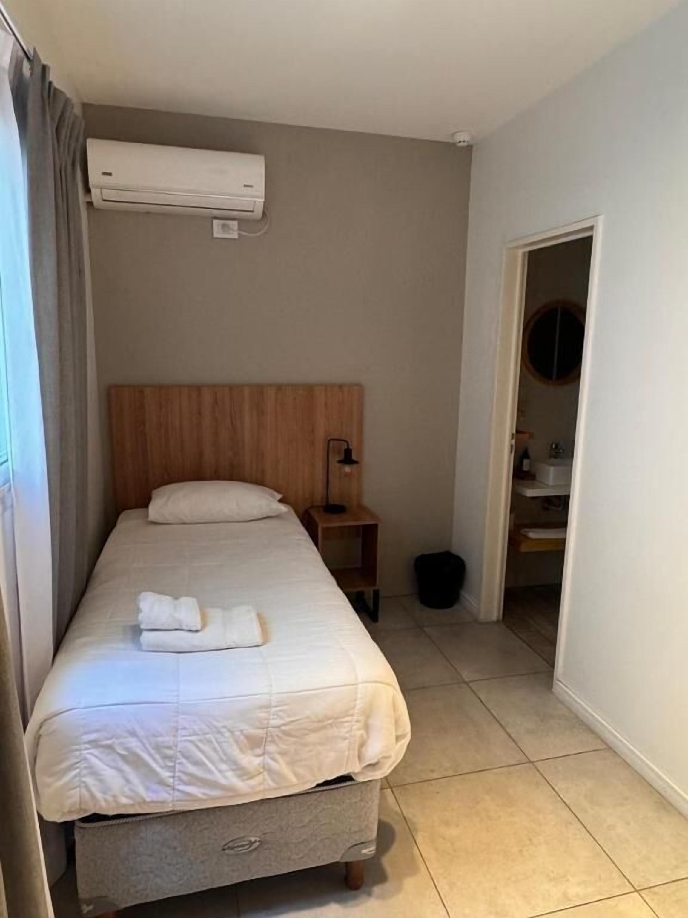 A single bed with a wooden headboard, a bedside table with a lamp, and an air conditioning unit mounted on the wall.