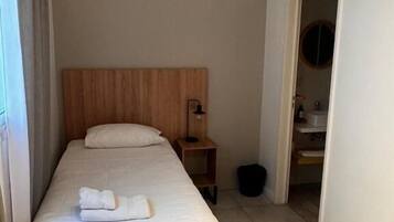 A single bed with a wooden headboard, a bedside table with a lamp, and an air conditioning unit mounted on the wall.