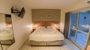 Habitación de hotel con una cama grande, un televisor de pantalla plana en la pared, una ventana con cortinas y una mesita con lámpara.