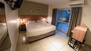 A bedroom with a bed, bedside lamps, a desk, and an air conditioning unit. - Casa Be Suites (Rosario)
