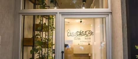 Entrada de un hotel con puerta de vidrio, una escalera en el interior y un letrero que dice "CASA CASA Be Suites".