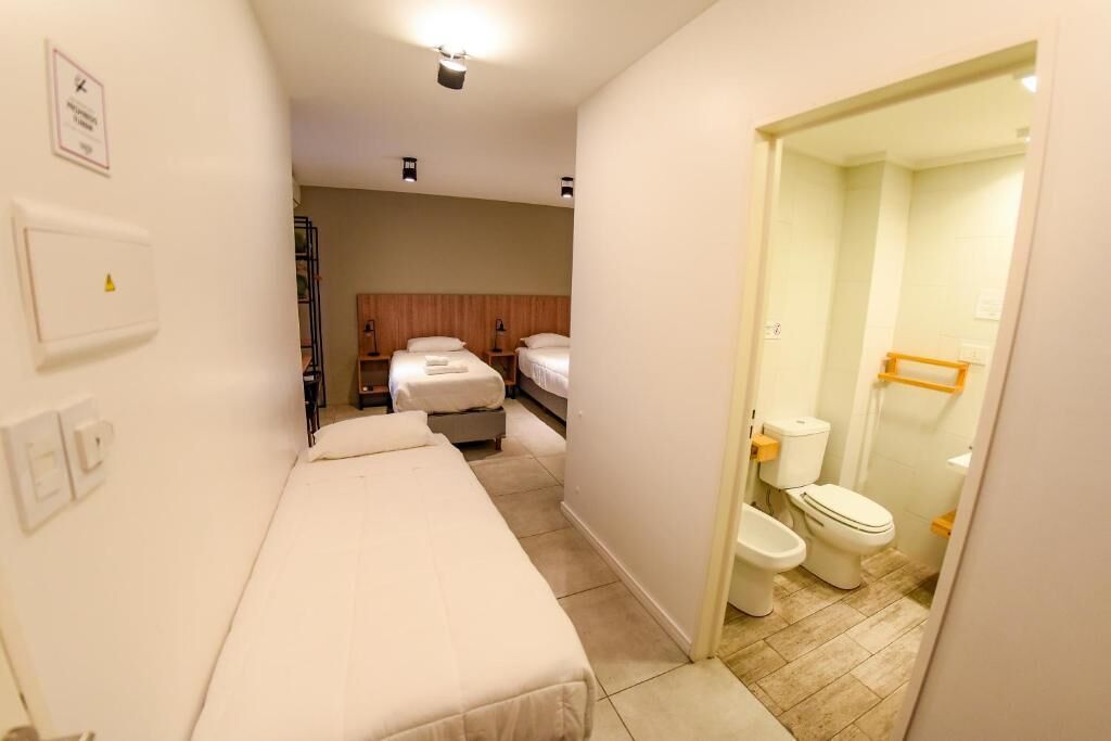 A hotel room with two beds, a small kitchenette, and a bathroom with a toilet and bidet.