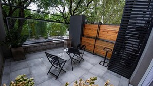An outdoor patio with a table and chairs, a wooden fence, and a view of trees and a street. - Casa Be Suites (Rosario)