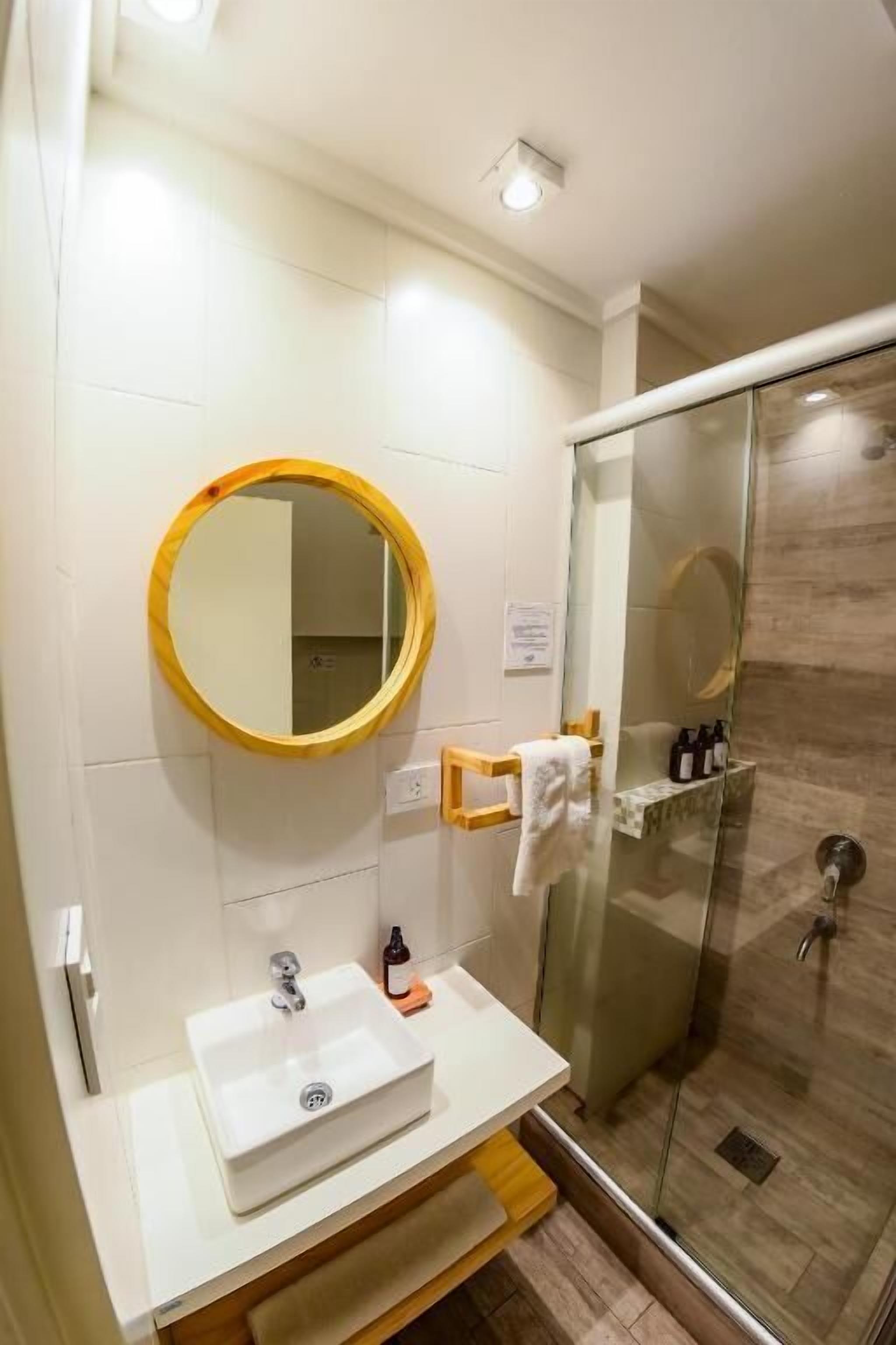 A bathroom with a white sink, a round mirror, and a glass-enclosed shower.