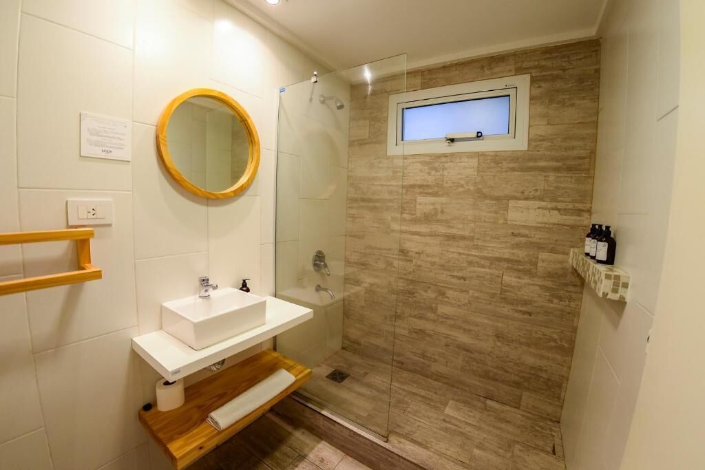 A bathroom with a white sink, a wooden vanity, a glass shower enclosure, and a small window.