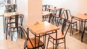 A modern cafe interior with wooden tables and black metal chairs, large windows, and hanging pendant lights. - Casa Be Suites (Rosario)