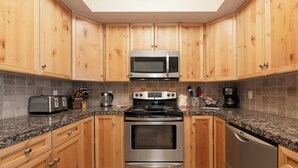 Eine moderne Küche mit Holzausstattung, einer Mikrowelle, einem Herd, einem Backofen und einem Geschirrspüler aus Edelstahl.