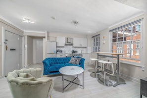 A modern kitchen with white cabinets and a blue sofa. There is a round table with a white top and metal legs. - 2 Bedroom Flat, Paddington, Central London (London)