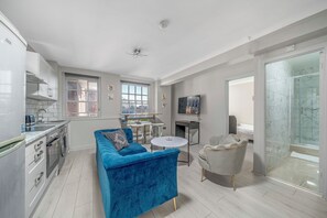 A modern kitchen with white cabinets, a blue sofa, a grey armchair, and a small round table. - 2 Bedroom Flat, Paddington, Central London (London)