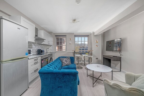 A modern kitchen with white cabinets, a blue sofa, and a dining area with a round table. - 2 Bedroom Flat, Paddington, Central London (London)