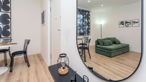 Ein modernes Wohnzimmer mit einem grünen Sofa, einem Essbereich mit Tisch und Stühlen und einem großen Spiegel, der den Raum widerspiegelt.