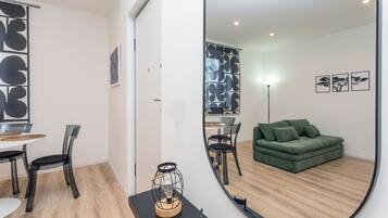 Ein modernes Wohnzimmer mit einem grünen Sofa, einem Essbereich mit Tisch und Stühlen und einem großen Spiegel, der den Raum widerspiegelt.