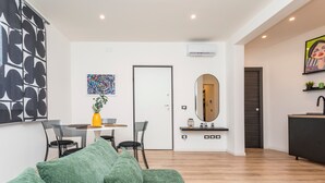 Ein modernes Wohnzimmer mit einem grünen Sofa, einem Essbereich mit Tisch und Stühlen, einem großen Spiegel und einer Küchenzeile mit Spüle und Arbeitsfläche.