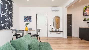 Ein modernes Wohnzimmer mit einem grünen Sofa, einem Essbereich mit Tisch und Stühlen, einem großen Spiegel und einer Küchenzeile mit Spüle und Arbeitsfläche.