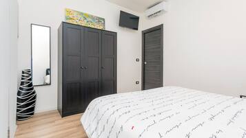 Ein Schlafzimmer mit Bett, Kleiderschrank, Fernseher und Kunstwerk an der Wand.