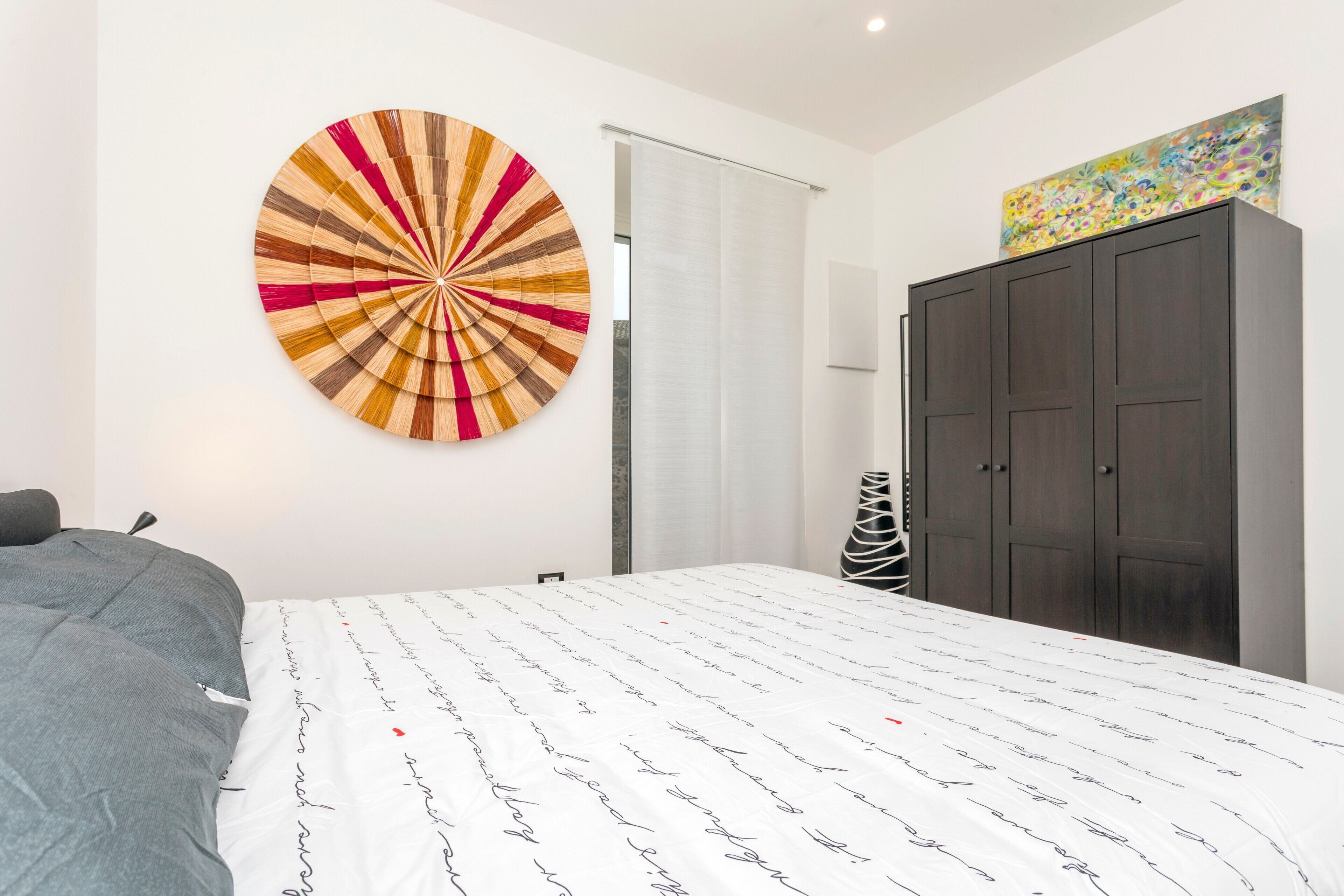 Une chambre moderne avec un lit, une grande œuvre d’art de forme circulaire, une armoire et une porte.