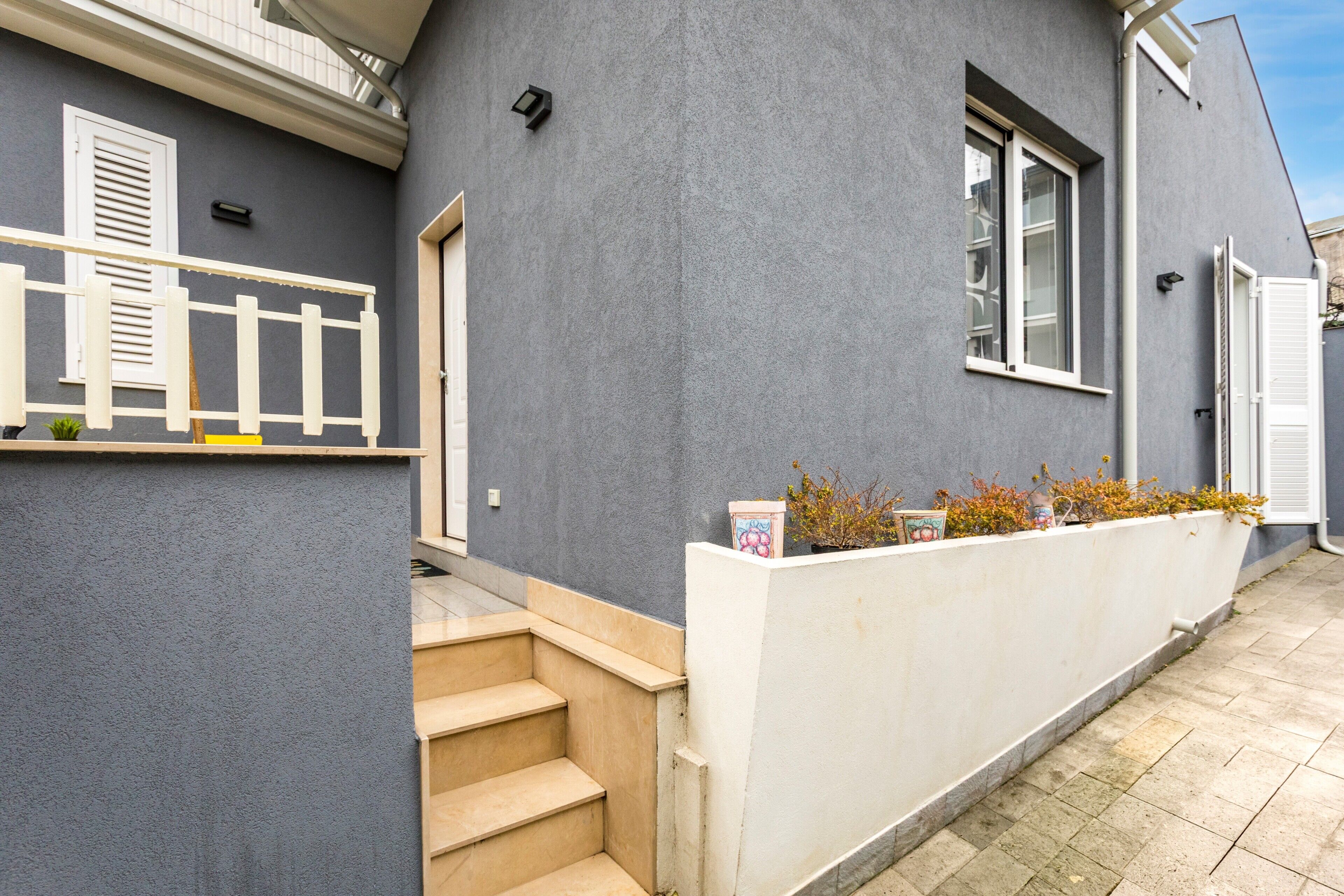 A grey building with a white exterior wall, a set of beige stairs, and a small planter with yellow flowers.